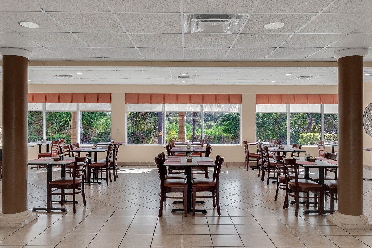 An empty dining area with neatly arranged tables and chairs, featuring large windows.