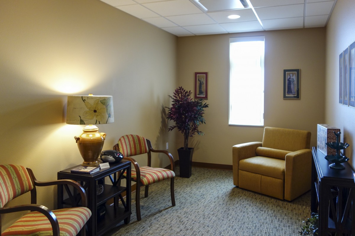 A cozy waiting room with comfortable chairs, a lamp, potted plant, and wall art.