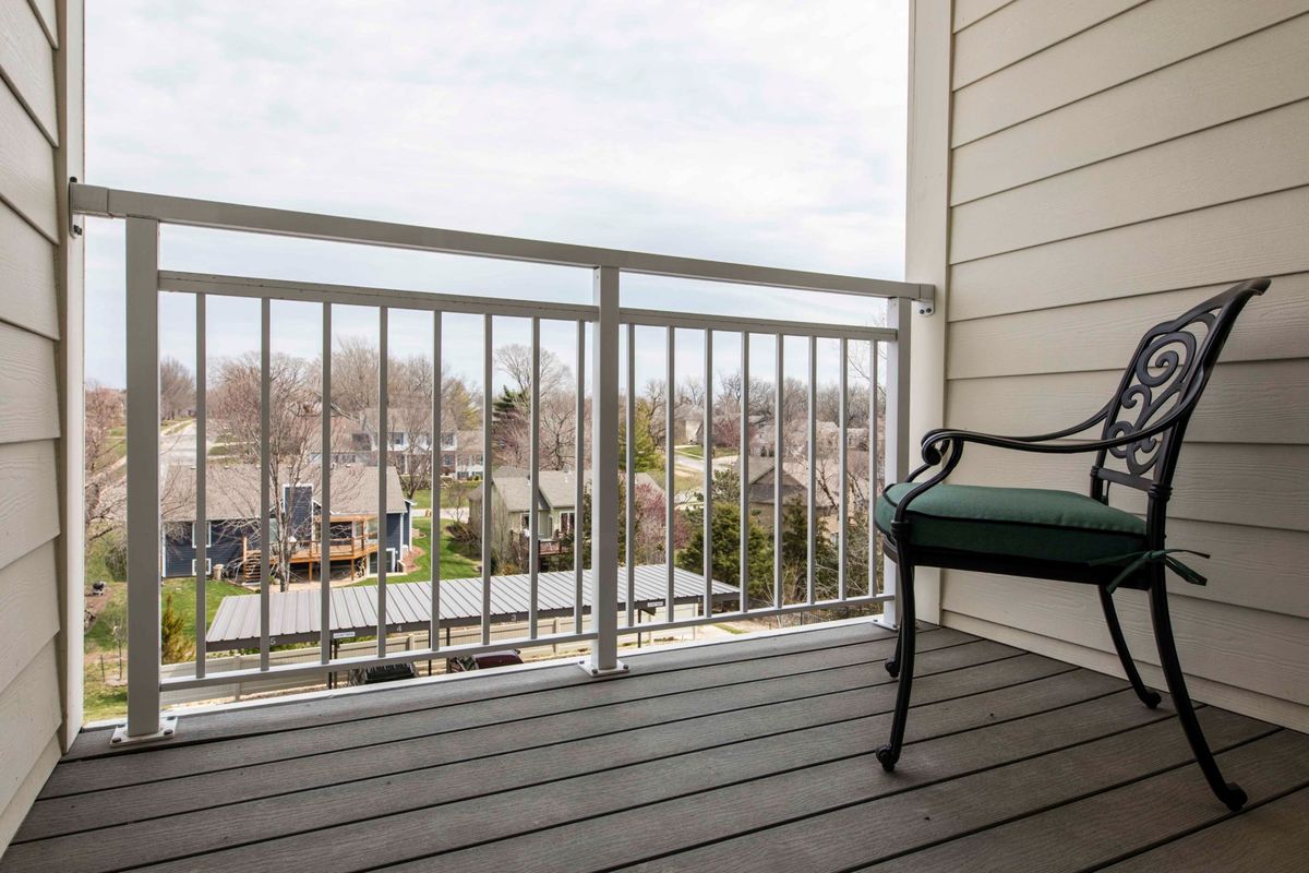 A residential balcony with a bench overlooking a suburban neighborhood.