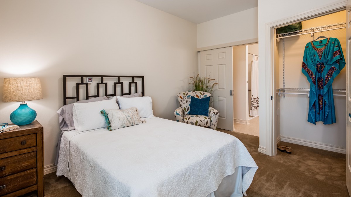 A cozy bedroom with a neatly made bed, a patterned armchair, and decorative pillows.