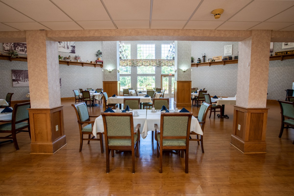 A spacious dining room featuring neatly arranged tables and chairs, with large windows providing ample natural light and decorative shelves enhancing the ambiance.
