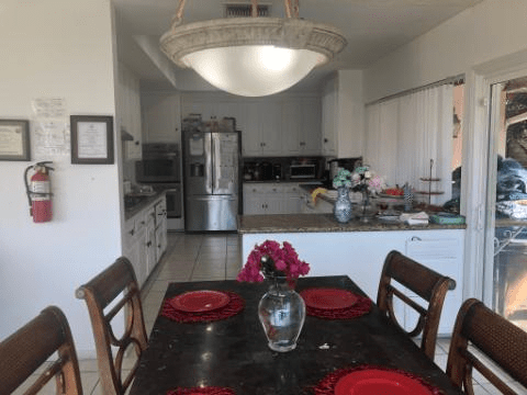 A view of a kitchen with a dining area featuring a table set with red plates and a vase of flowers.