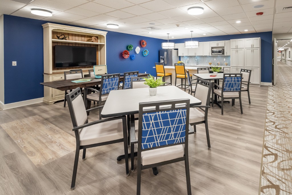 A modern dining area with several tables and chairs, featuring a kitchenette and decorative wall art.