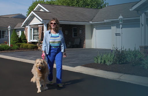 A woman walking her golden retriever in front of a quaint house.