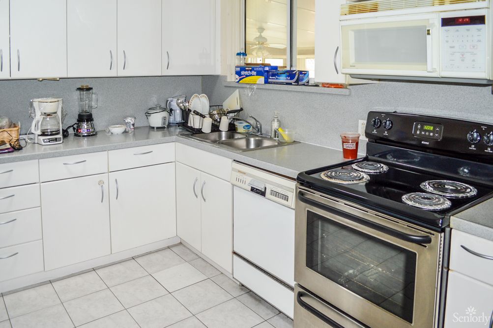 A modern kitchen with white cabinets, featuring a stove, dishwasher, and microwave.