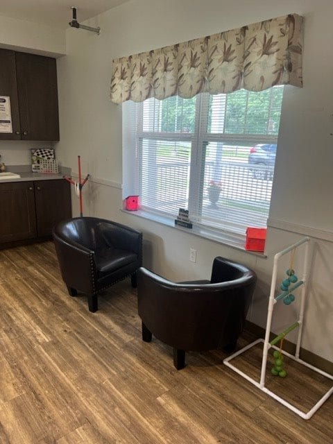 A cozy waiting area with two black chairs by a window and a kitchenette nearby.