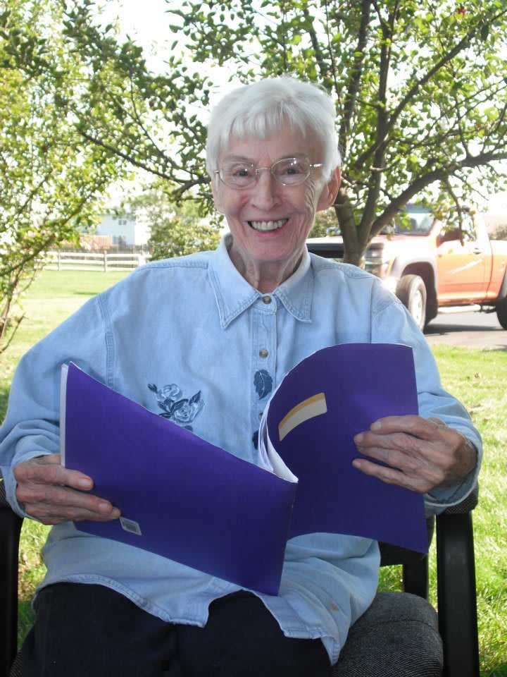 An elderly person sitting outdoors, enjoying reading a book and smiling.