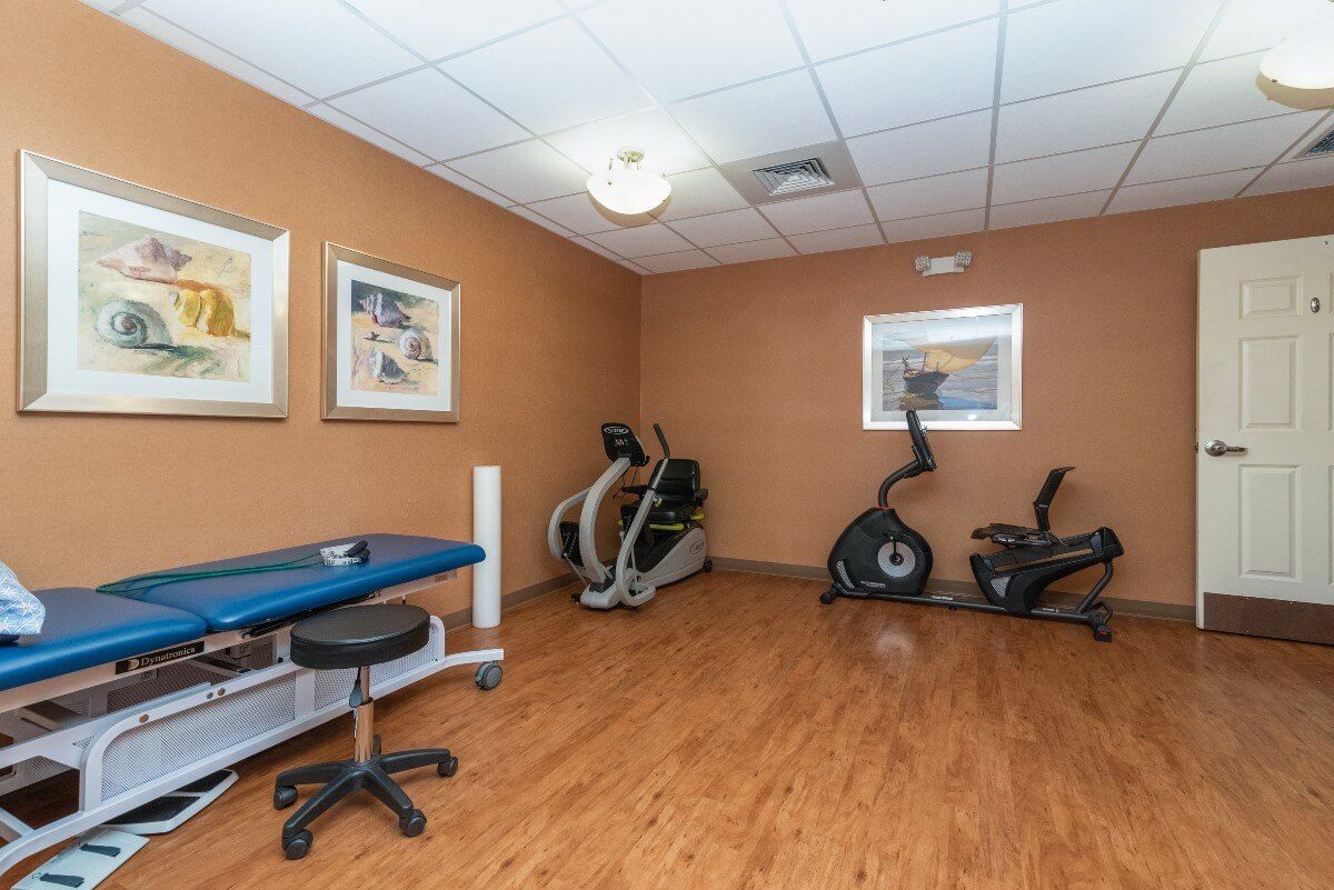 A small exercise room featuring various gym equipment including stationary bikes and an exam table, with framed artworks on the walls.