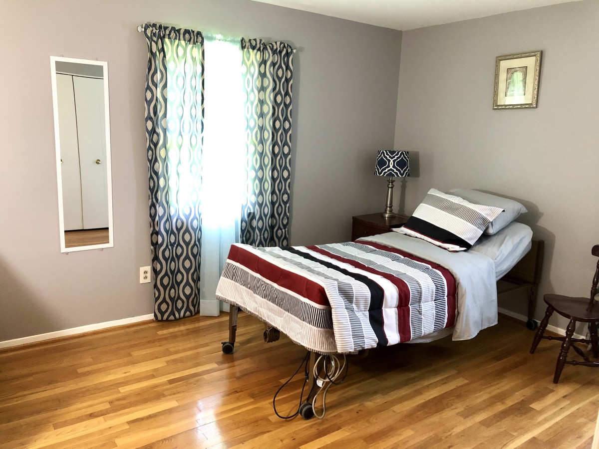 A simple bedroom with a single bed, striped bedding, and hardwood floors.