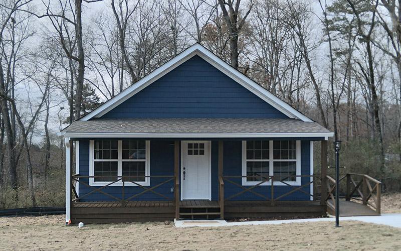 A single-story blue house with a porch, surrounded by trees.