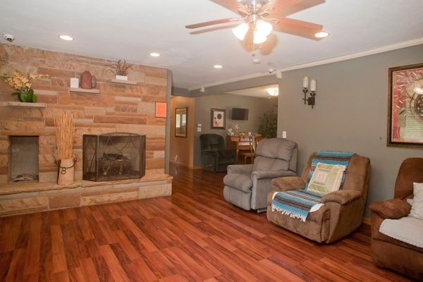 A cozy living room with hardwood floors, a fireplace, and recliner chairs under a ceiling fan.
