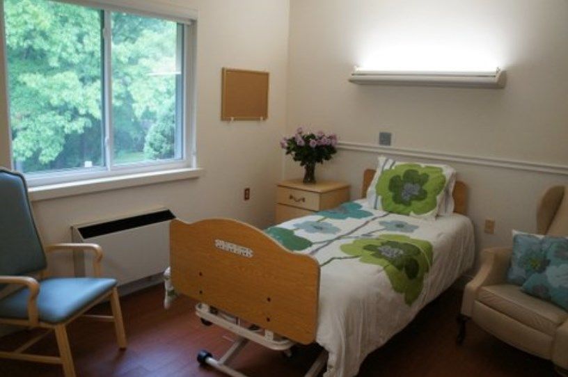 A hospital room with a single bed, window, and flowers on a bedside table.