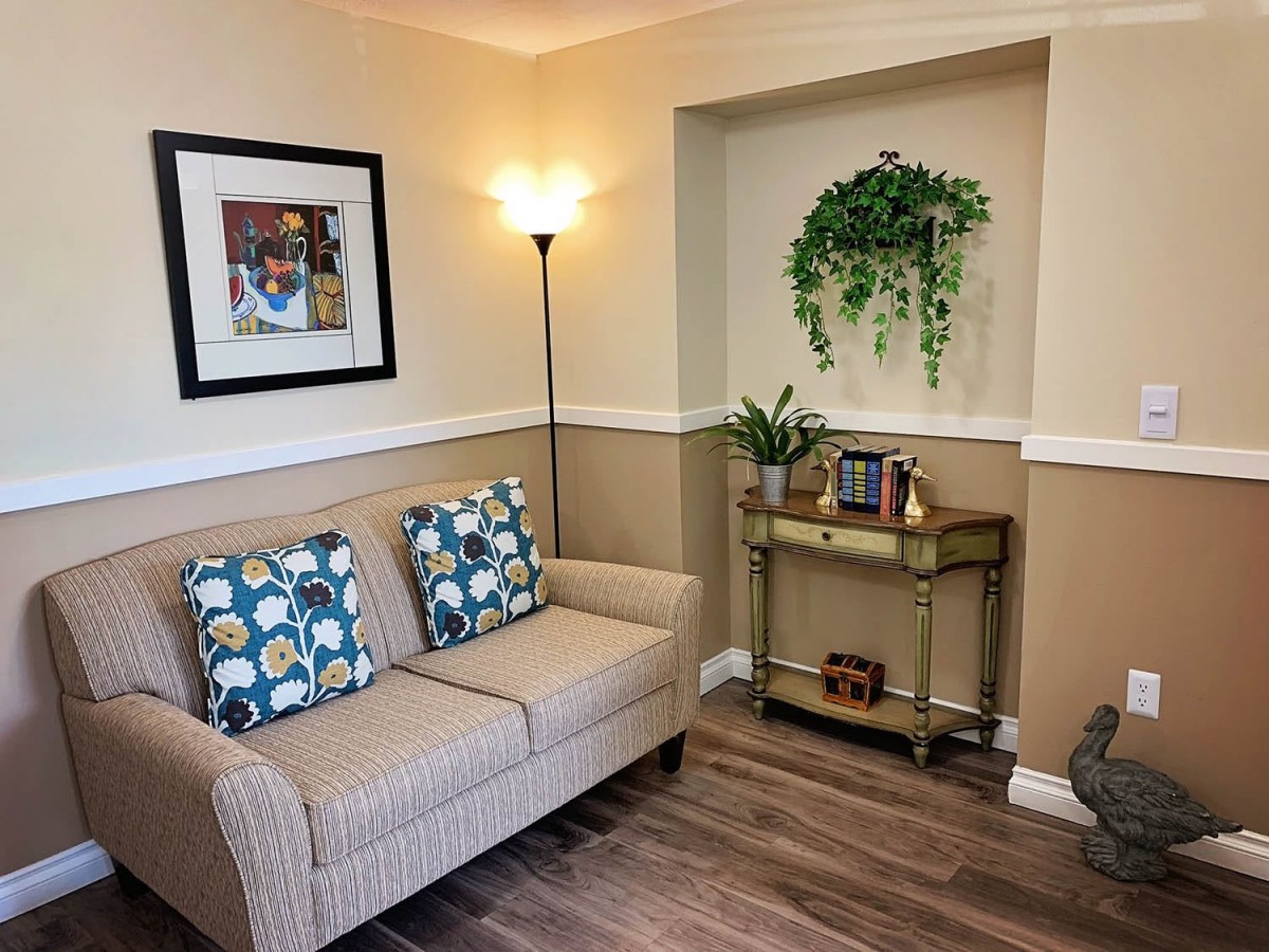 A cozy living room corner with a sofa, decorative pillows, artwork on the wall, and plants on a side table.