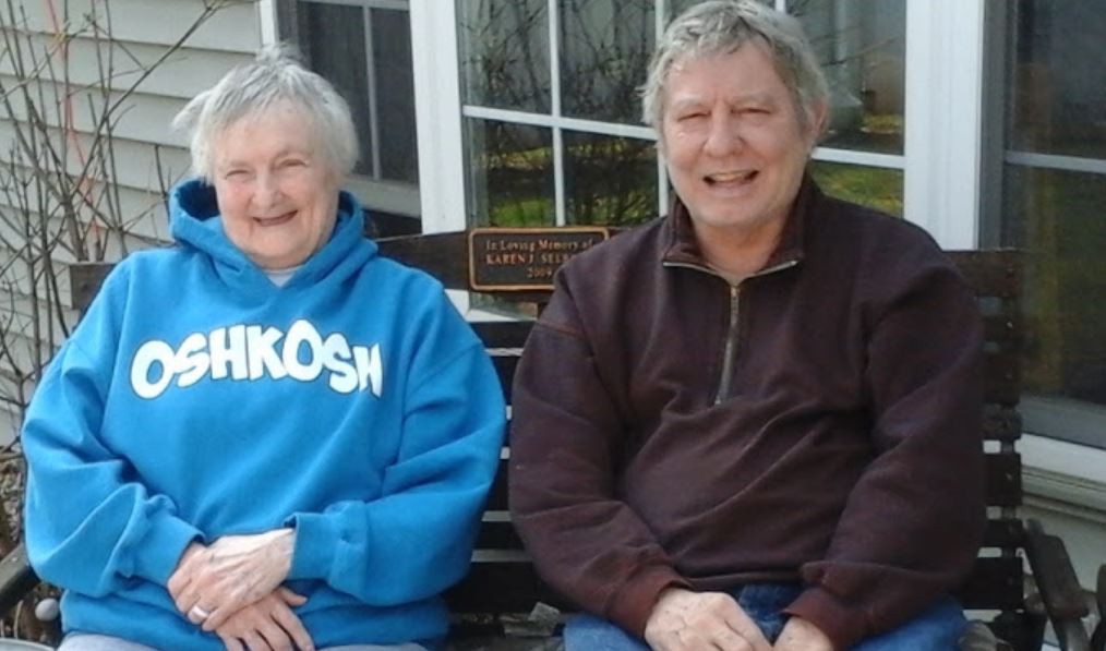An elderly couple sitting on a bench outdoors, smiling and enjoying their time together.