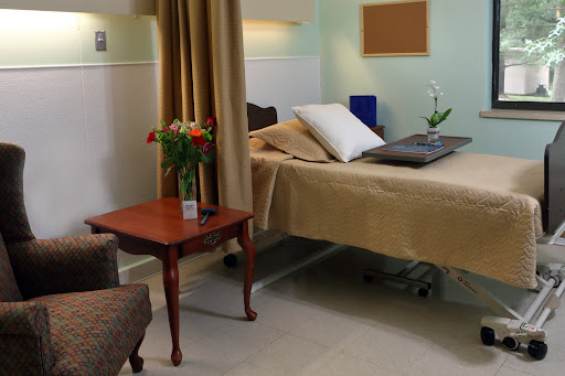 A serene hospital room featuring a bed, a small table with flowers, and comfortable seating.