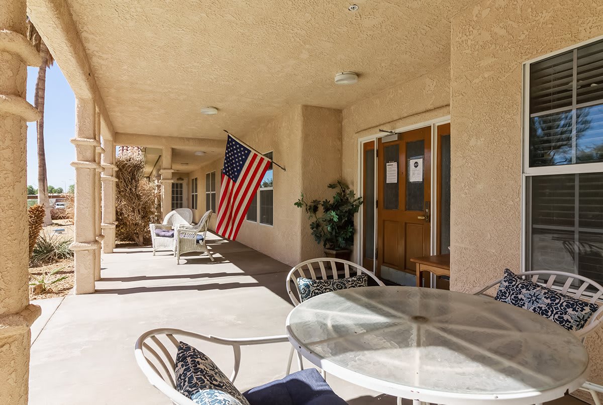 A covered outdoor patio with a seating area, featuring a glass table and chairs, and displaying an American flag.