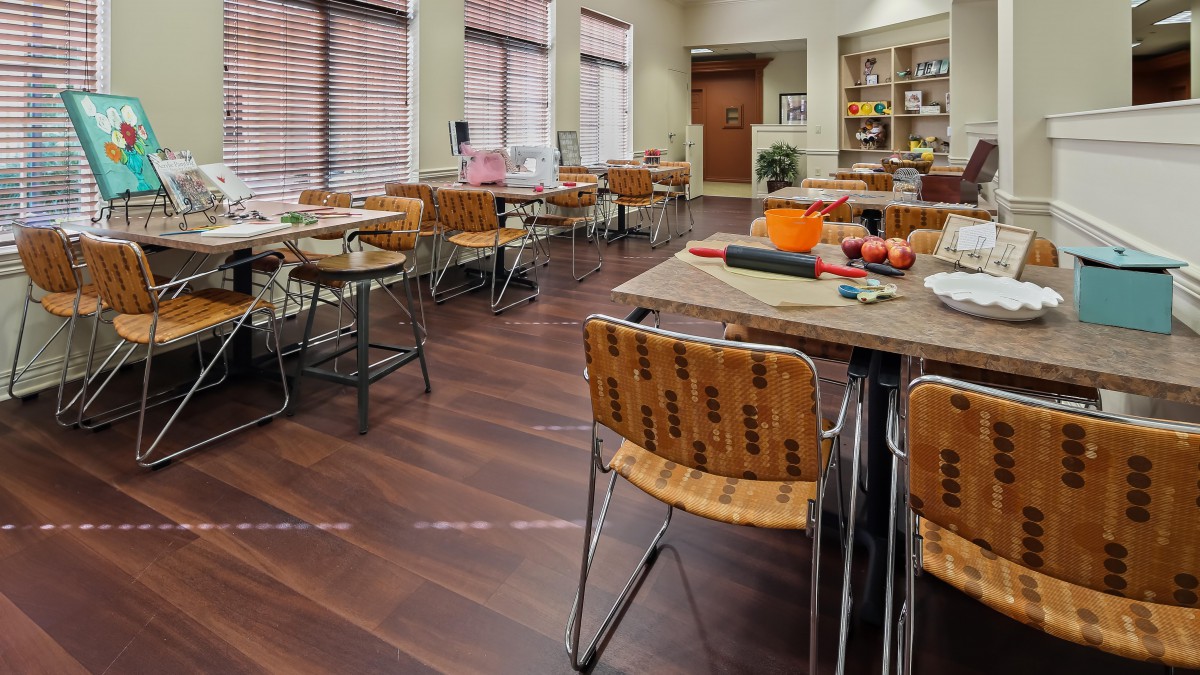 A cozy dining area with wooden flooring, featuring neatly arranged tables and chairs near large windows.