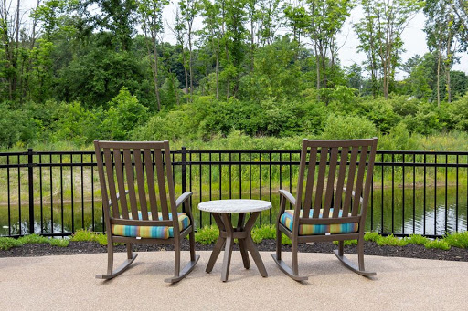 A serene outdoor seating area with two rocking chairs and a small table, surrounded by lush greenery.