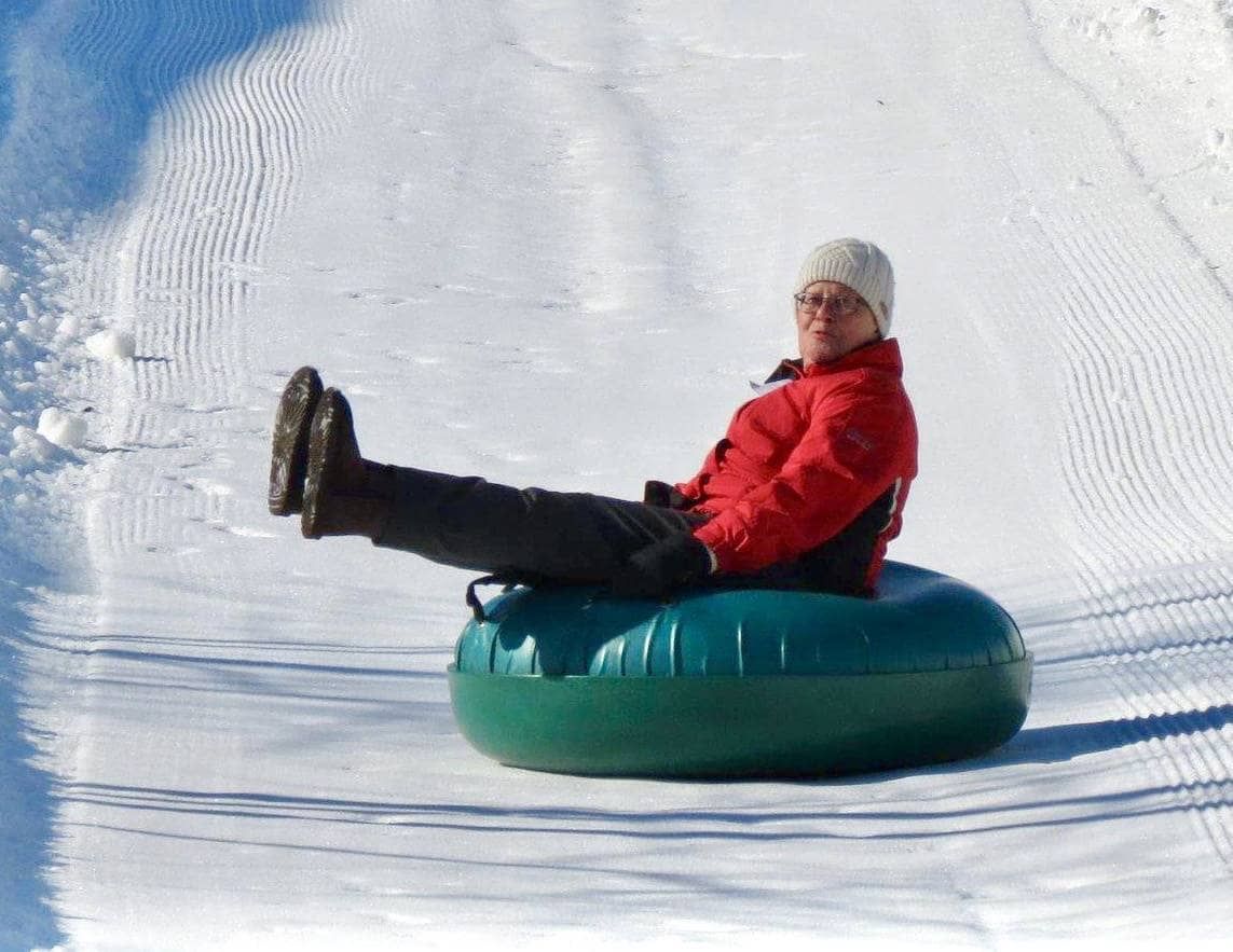 A person enjoying snow tubing on a sunny winter day.
