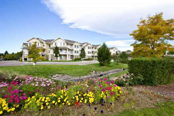 A scenic view of a well-maintained apartment complex with vibrant flower gardens and neatly trimmed lawns.