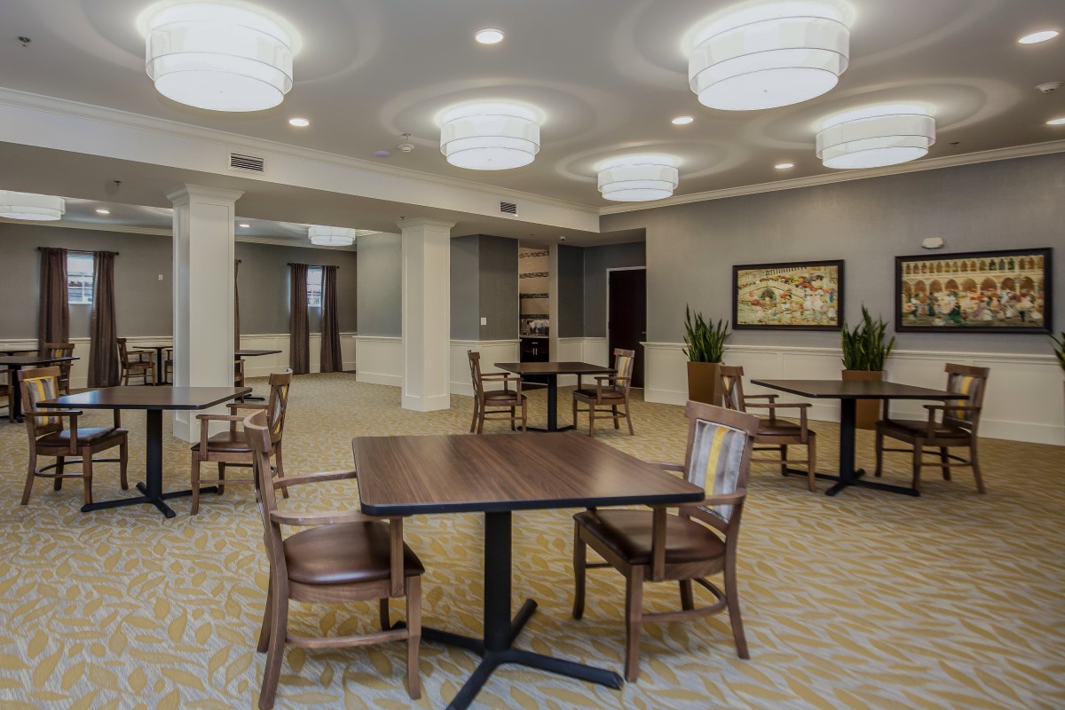 A spacious and well-lit room featuring tables, chairs, and modern lighting fixtures.
