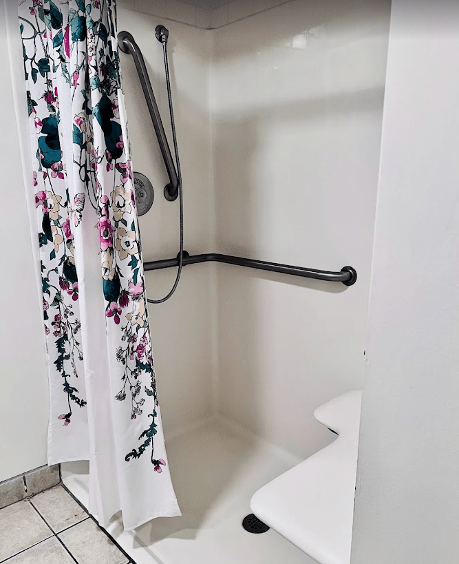 A bathroom shower area with a floral curtain and accessibility grab bars.
