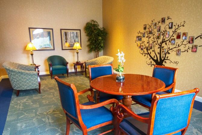 A cozy lobby seating area with a wooden table and blue upholstered chairs, decorated with indoor plants and wall art.