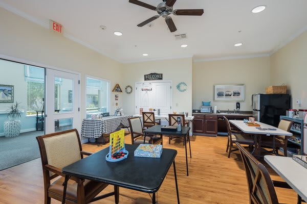 A well-lit room with tables and chairs, featuring a ceiling fan and decorative items.
