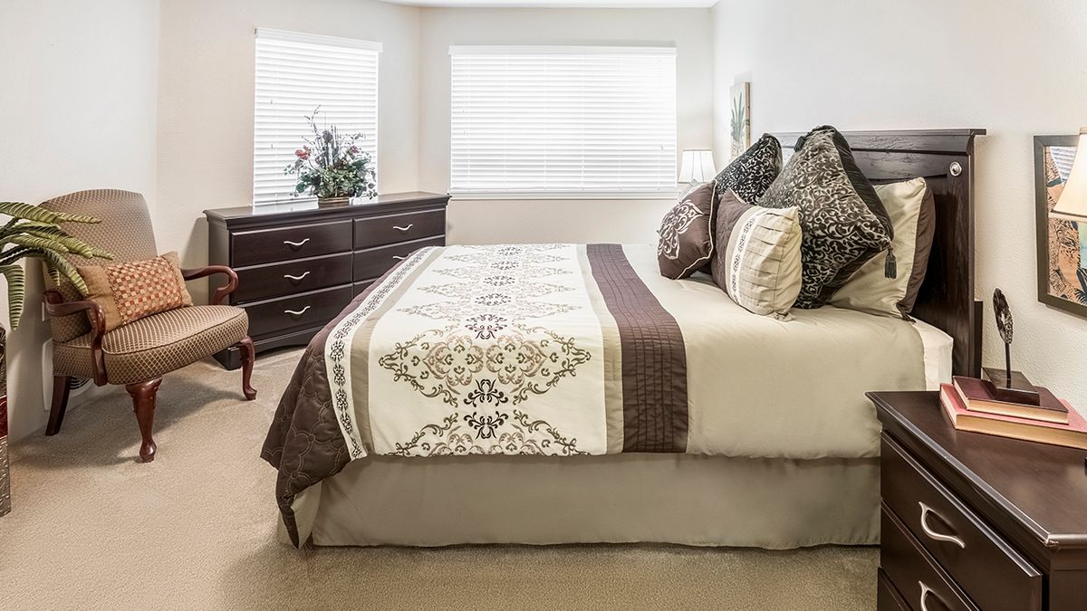 A well-decorated bedroom with a bed, pillows, dresser, and window.