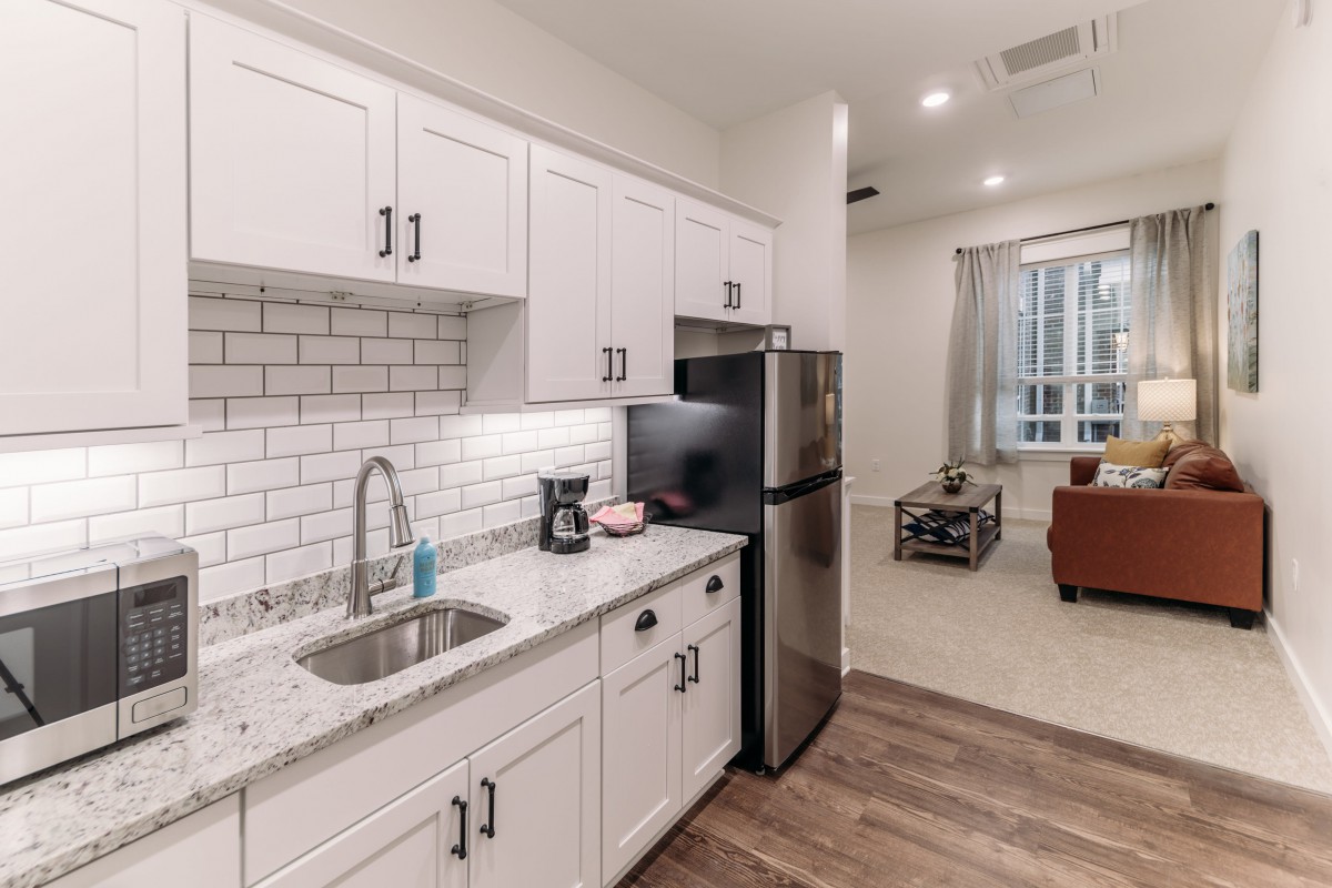A modern kitchen with white cabinets and subway tile backsplash, opening to a cozy living room.