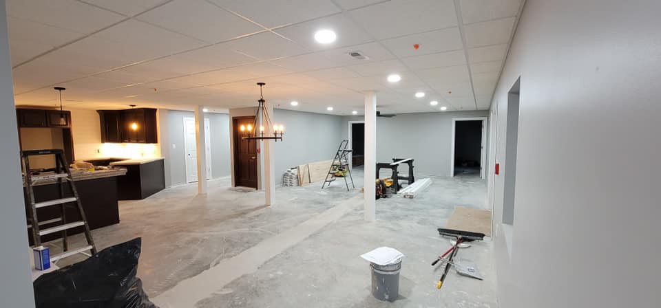 An unfinished basement under renovation with ceiling lights and various construction tools.