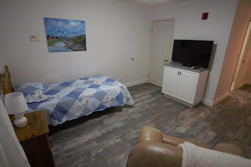 A minimalist bedroom with a single bed, television, and artwork on the wall.