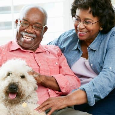A cheerful couple sitting indoors with their fluffy dog, enjoying a moment of togetherness.