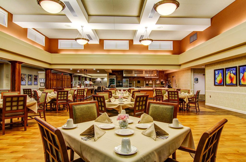 An elegant dining room with neatly arranged tables and chairs, featuring soft lighting.