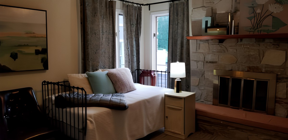 A cozy bedroom with a daybed beside a window, adorned with pillows and illuminated by a table lamp.