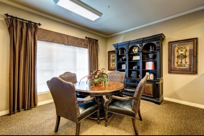 A cozy office meeting room with a round table, four chairs, and a bookshelf.