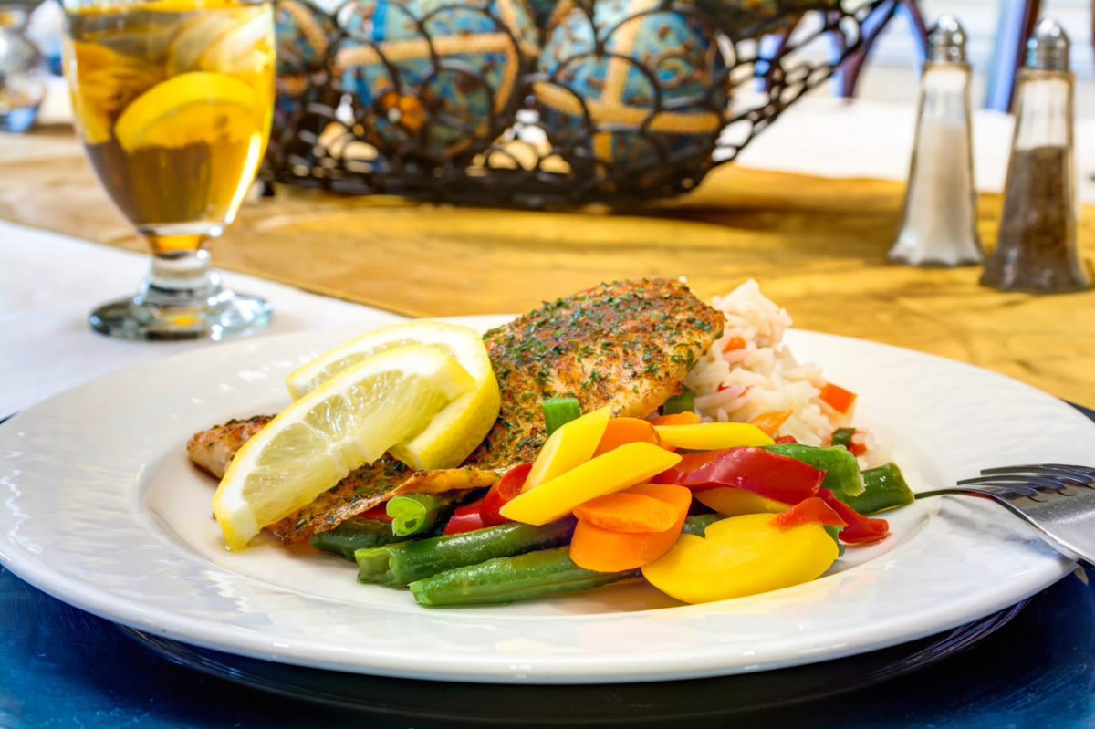 A beautifully plated salmon dish with mixed vegetables and lemon slices, served on a dining table.