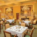 An elegant restaurant dining room with chandeliers and neatly set tables.