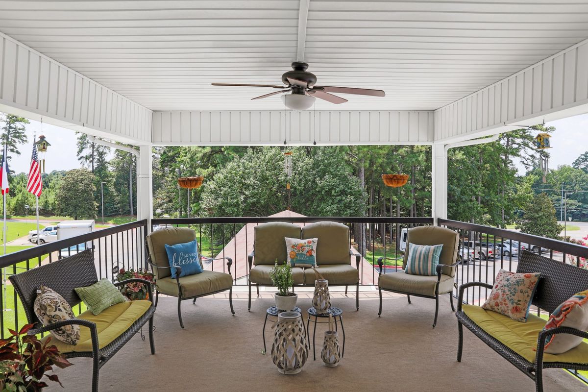 A cozy porch with cushioned seating and a ceiling fan, overlooking a lush green yard.