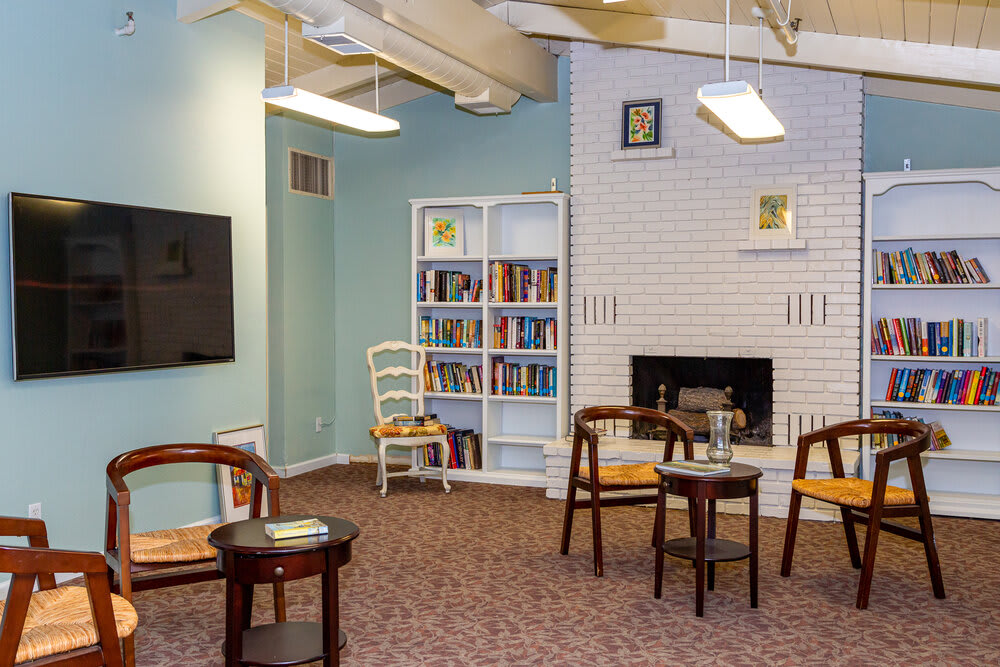 A cozy reading area with a white bookshelf, chairs, and a fireplace.