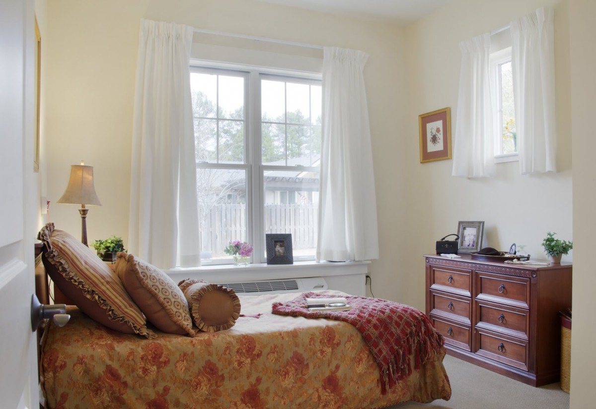 A cozy bedroom with a large window, bed, and dresser.