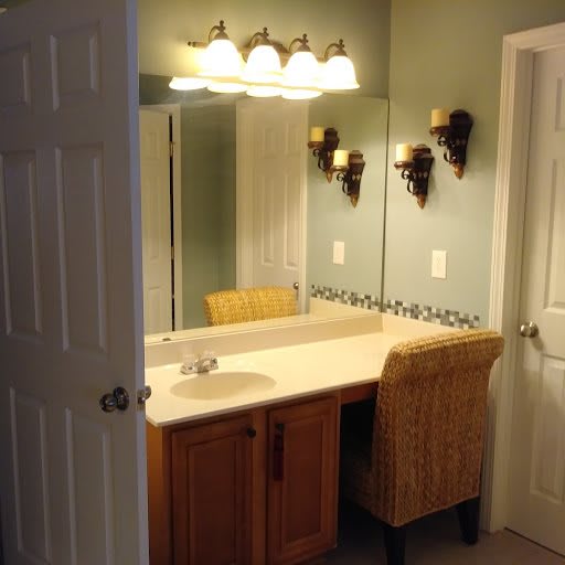 A bathroom vanity with a large mirror, overhead lights, and a wicker chair.