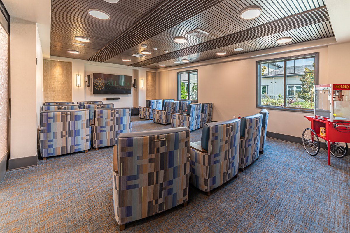 A modern lounge area with patterned seating arranged around a television, featuring ample natural light and contemporary decor.