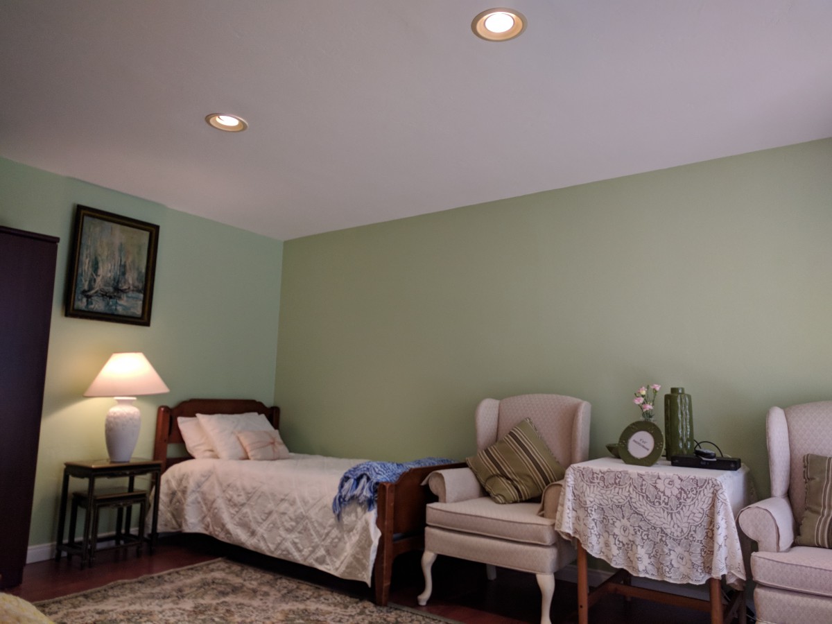 A cozy bedroom with a single bed, an upholstered chair, and a small table adorned with a lamp.
