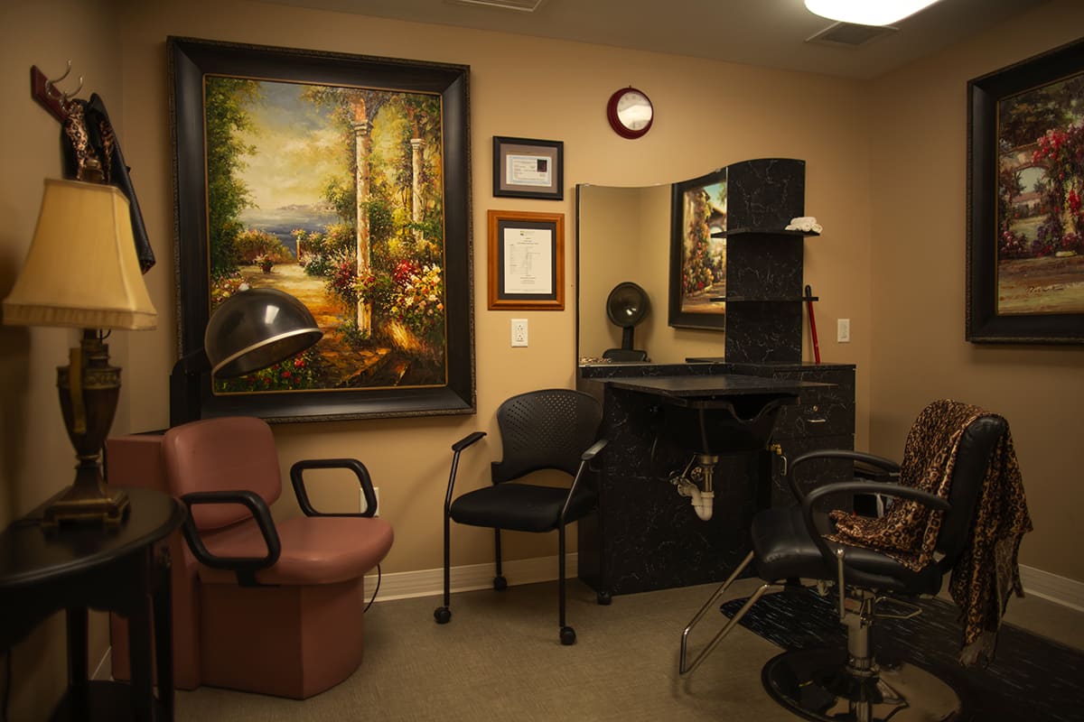 A cozy hair salon interior featuring chairs, a mirror, and decorative artwork on the wall.
