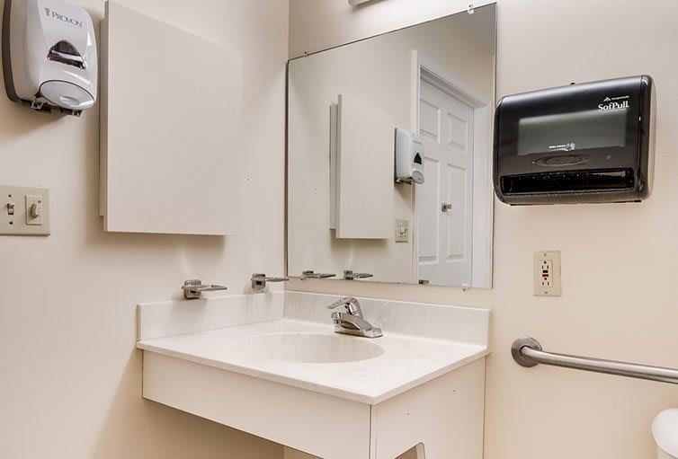 A clean bathroom with a sink and mirror, featuring a paper towel dispenser on the wall.