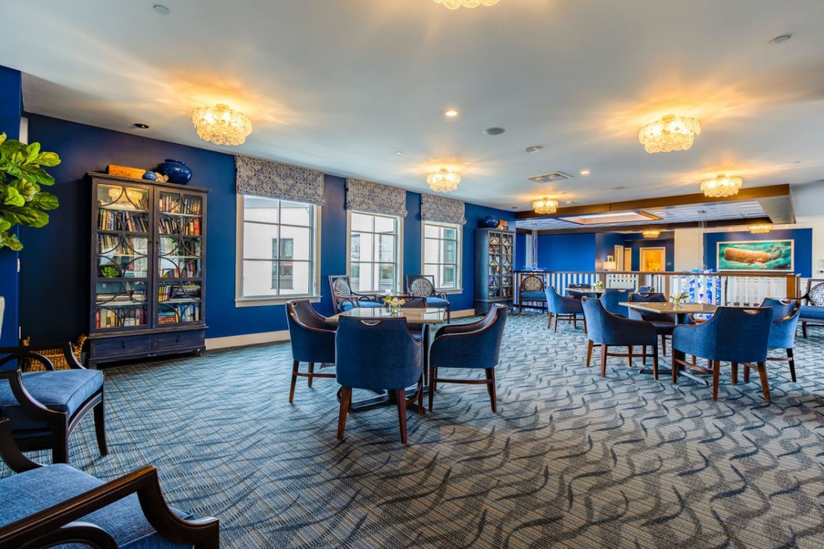 A spacious lounge with blue walls, featuring elegant chandeliers, bookshelves, and comfortable seating.