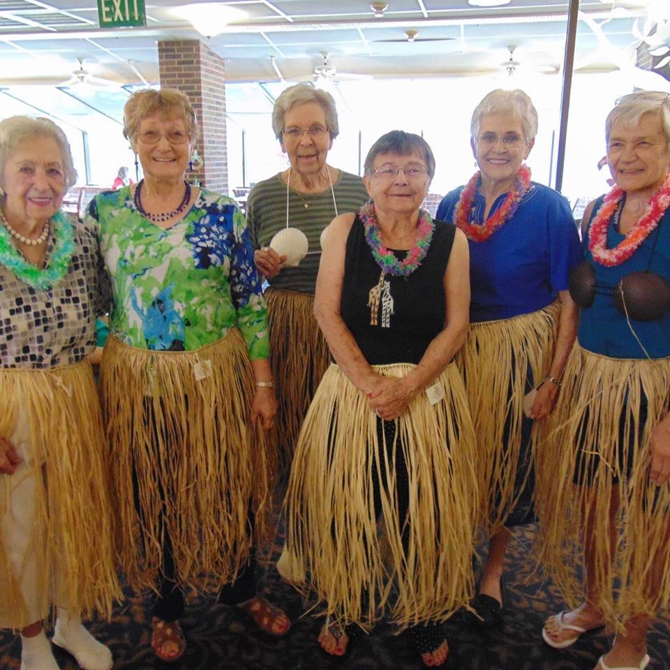 A group of women dressed in hula skirts and leis, possibly at a themed event.