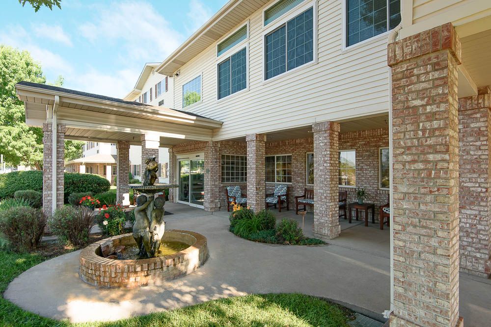 A well-maintained patio area with a fountain and garden outside a building with large windows.