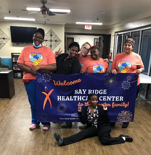 Staff members of Bay Ridge Healthcare Center celebrate together with a welcome banner during a community event.